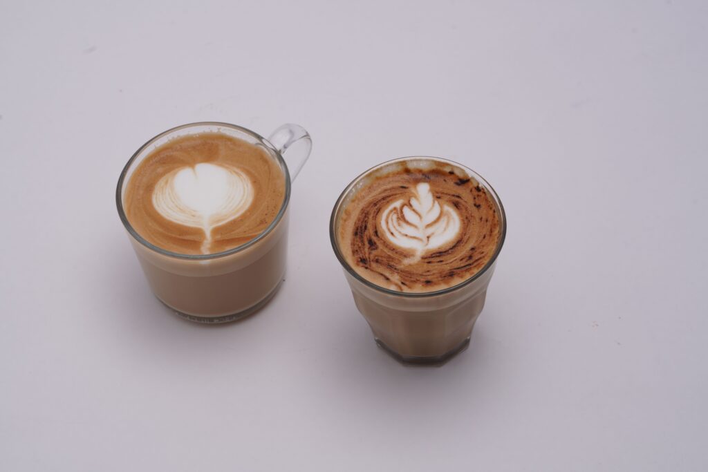 Two glass cups of latte with intricate latte art on white background.