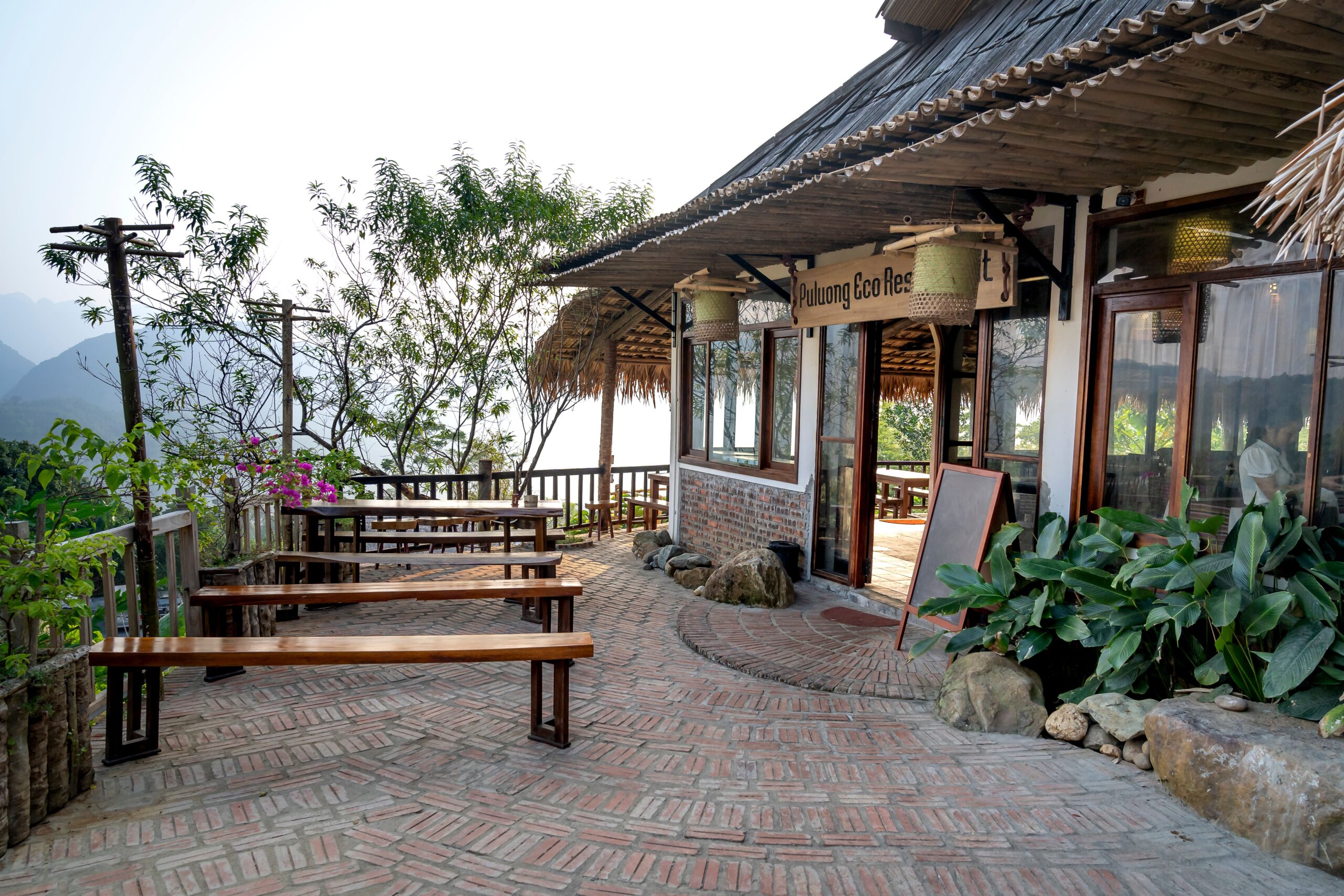 Exterior of small restaurant with wooden tables outside located on top of mountain in tropical terrain