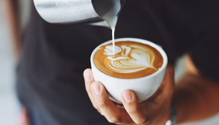 Close-up of a barista pouring milk to create latte art in a coffee cup.